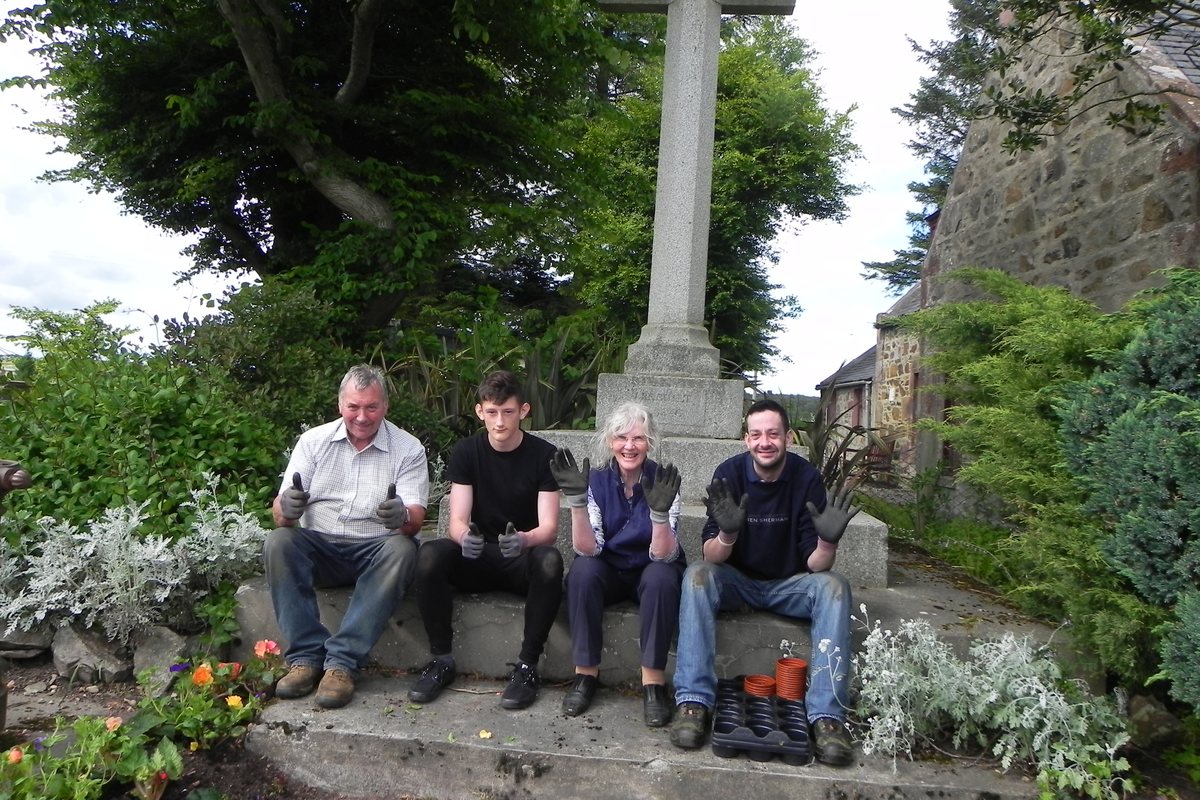 Four volunteers with gardening gloves at the village cross